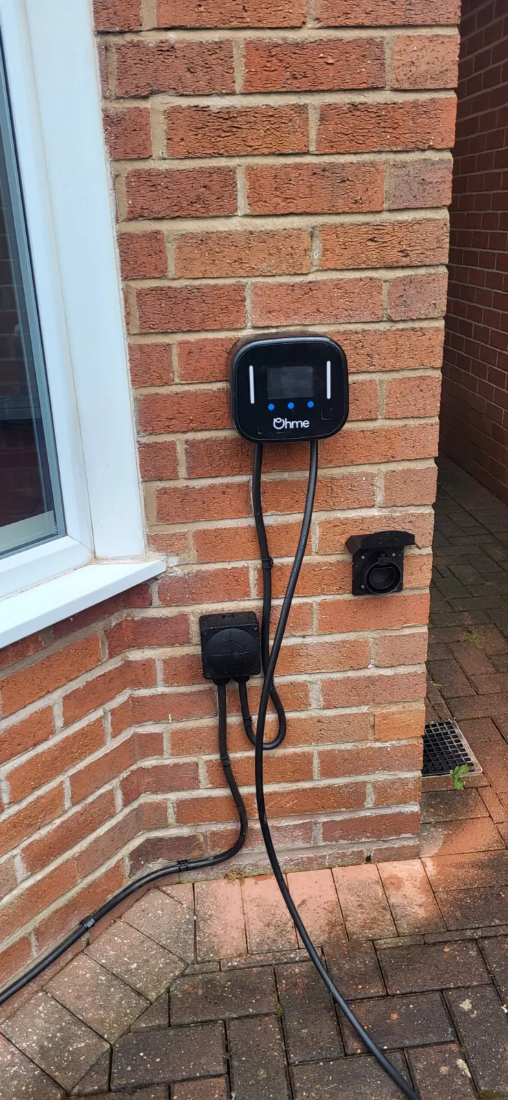 EV charge point installed on a brick wall beside a driveway