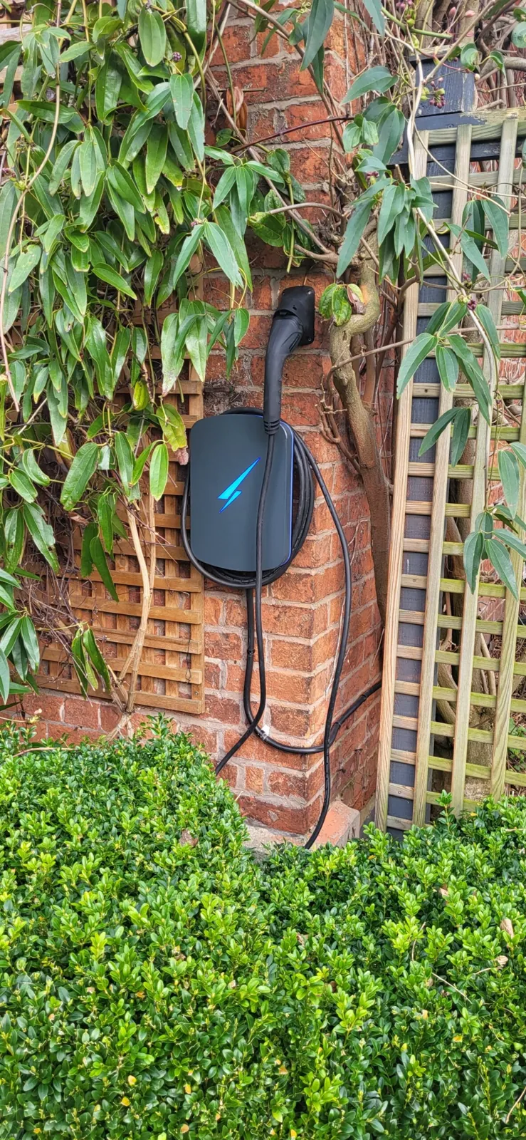 Wall mounted EV charge point installed on a brick wall beside a garden trellis