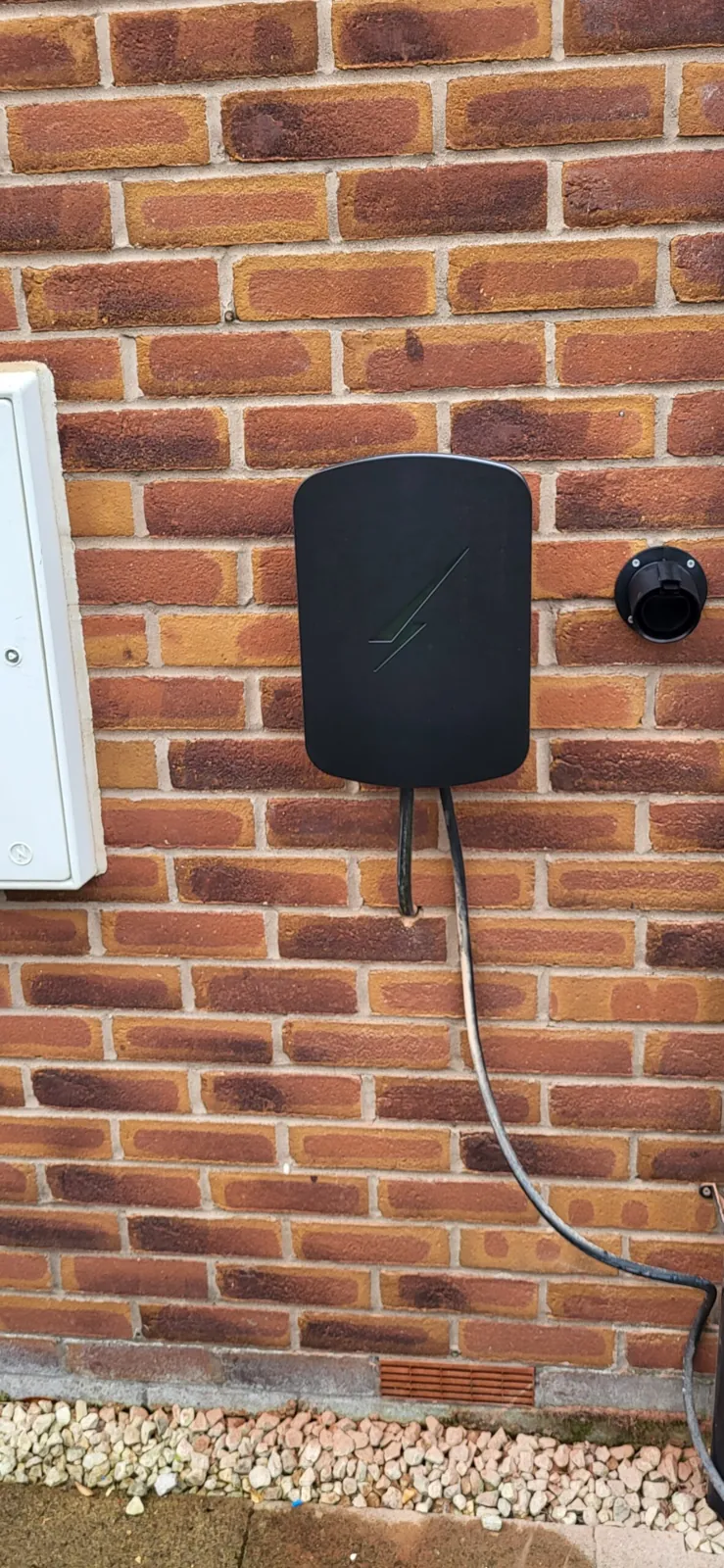 Wall mounted electric vehicle charger with tidy cable management on brick